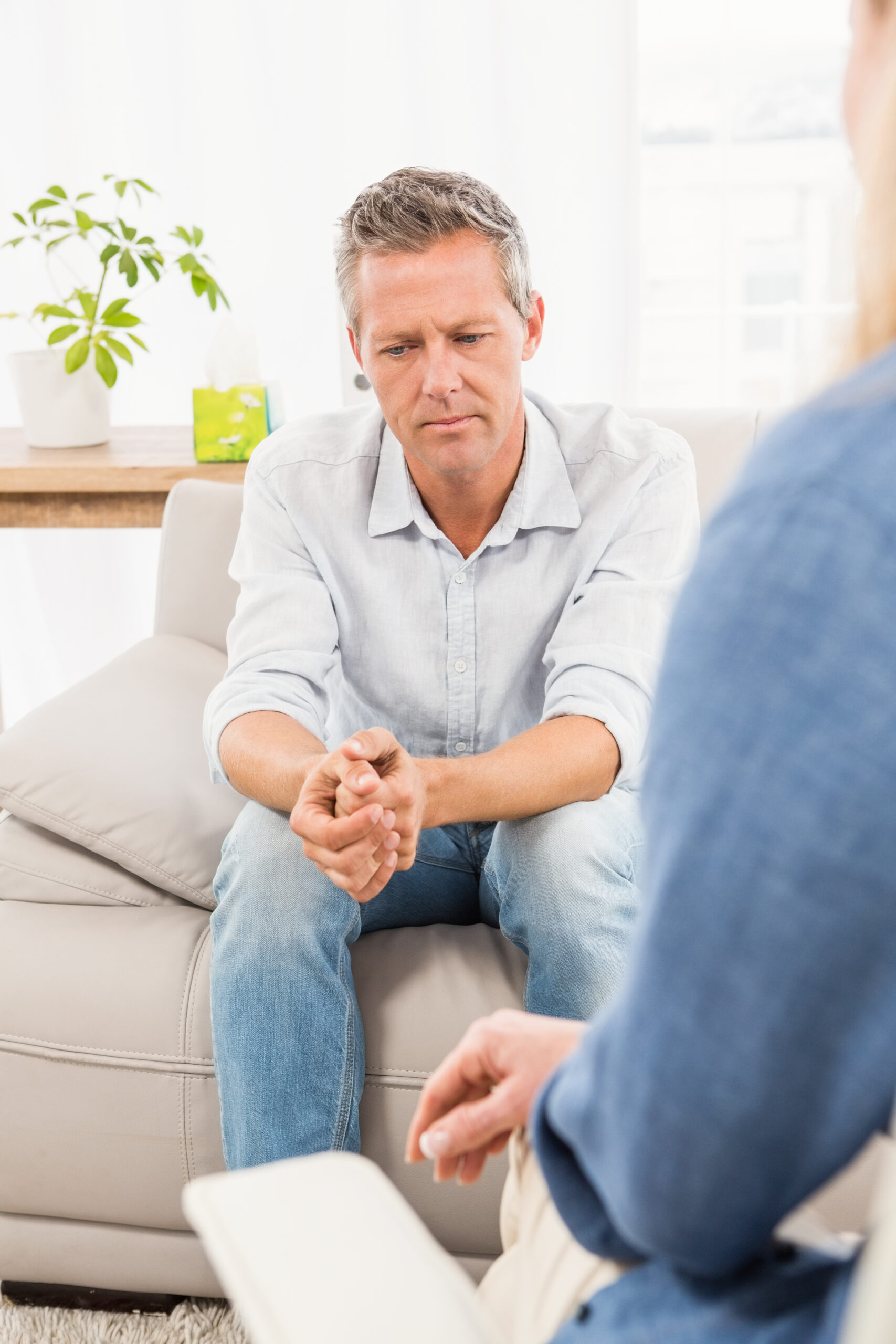 Worried man sitting on couch and talking to therapist in the office